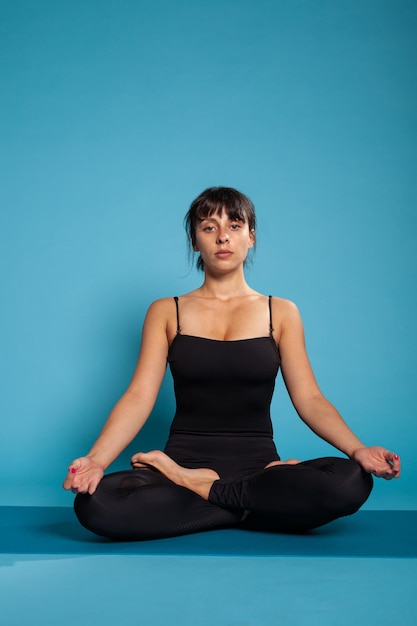 Entrenador personal sentado en una alfombra de yoga en posición de loto meditando durante el entrenamiento físico. Mujer atleta que trabaja en la postura corporal practicando la meditación espiritual. Concepto de ejercicio físico