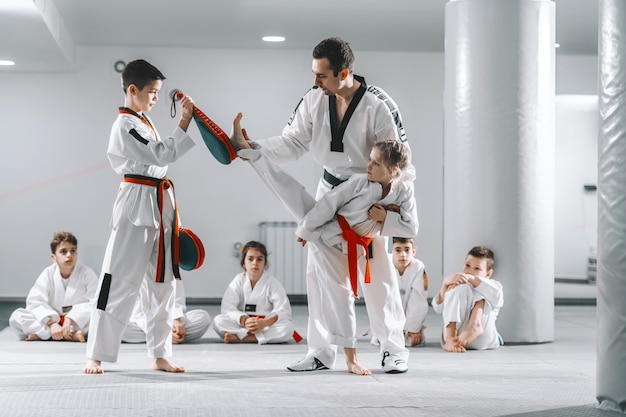 Foto entrenador que muestra a la niña cómo patear el objetivo. niño sosteniendo el objetivo. concepto de formación tekwondo.