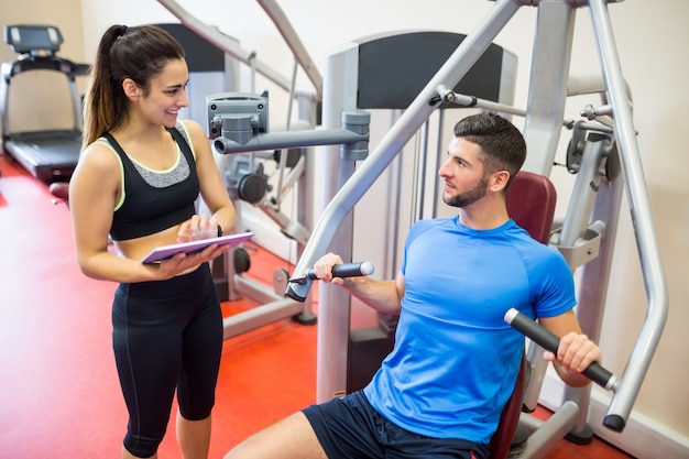 Entrenador que trabaja con atleta en la máquina de pesas