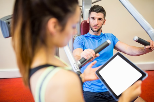 Entrenador que trabaja con atleta en la máquina de pesas