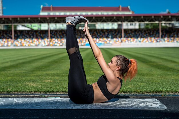 Entrenador de sexo femenino que hace ejercicio de yoga o pilates contra el fondo verde del estadio. Estilo de vida activo, saludable