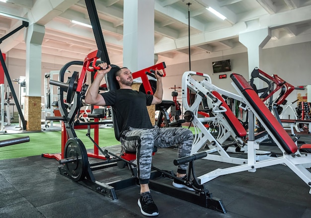 Entrenador sexy con prensa muscular en gran forma física realiza entrenamiento para clientes jóvenes