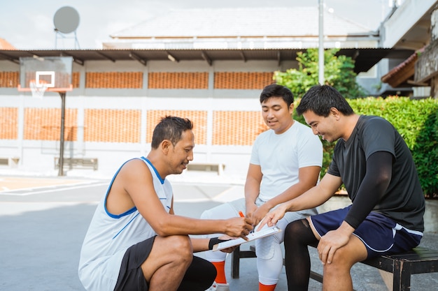 Un entrenador sostiene un portapapeles mientras instruye a dos jugadores de baloncesto