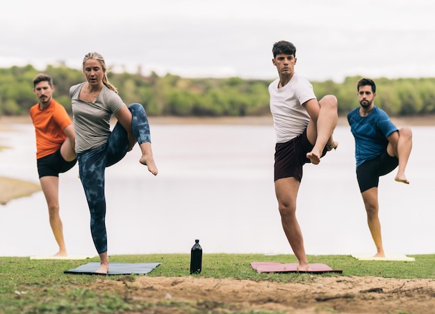 Entrenador de yoga femenino dirigiendo una clase de yoga con tres hombres junto a un lago en un parque