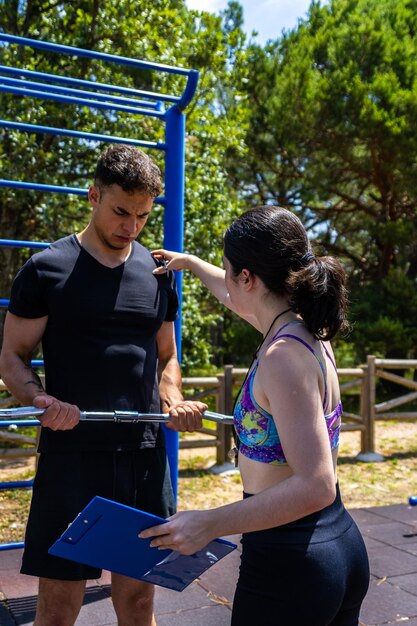 Entrenadora personal femenina corrigiendo la postura de un hombre mientras hace el ejercicio de curl de bíceps al aire libre