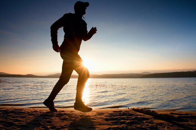 Entrenamiento al atardecer una silueta del cuerpo del corredor en el camino a lo largo de la costa del lago