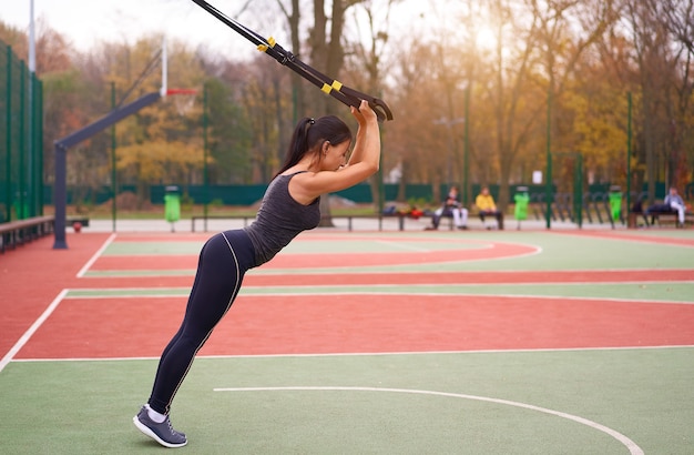 Entrenamiento de atleta chica usando trx en sportground