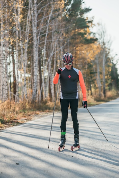 Entrenamiento de un atleta en los patinadores Biatlón Paseo en los esquís con bastones de esquí en el casco Entrenamiento de otoño Deporte de rodillos