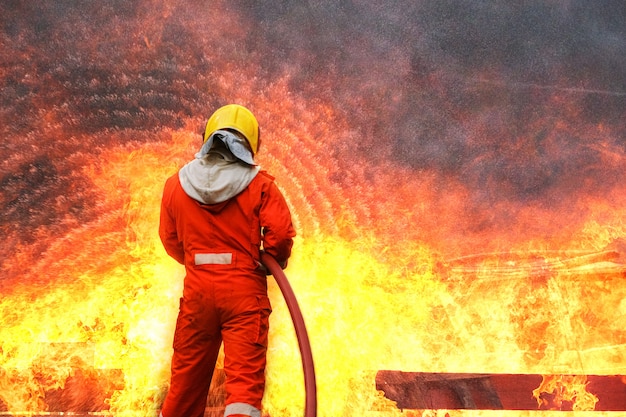 Entrenamiento de bomberos, práctica del equipo para luchar contra incendios en situaciones de emergencia. Un bombero lleva una manguera de agua a través de la llama