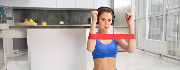 Foto entrenamiento en casa y bienestar centrado en una joven mujer fitness estirando banda elástica de resistencia con brazos