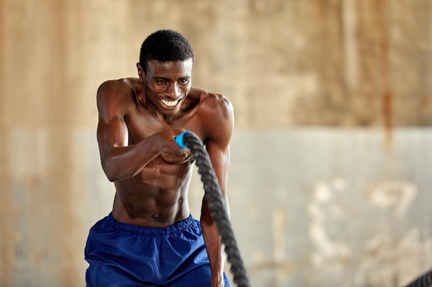 Entrenamiento de cuerda Hombre deportivo haciendo ejercicio de cuerdas de batalla al aire libre Atleta masculino negro haciendo ejercicio funcional con cuerda pesada