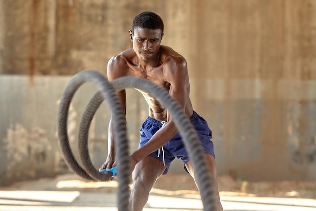 Entrenamiento de cuerda Hombre deportivo haciendo ejercicio de cuerdas de batalla al aire libre Atleta masculino negro haciendo ejercicio funcional con cuerda pesada