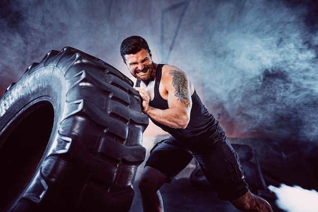 Entrenamiento de culturismo, deportista fuerte barbudo con cuerpo musculoso levantando ruedas pesadas en el gimnasio.