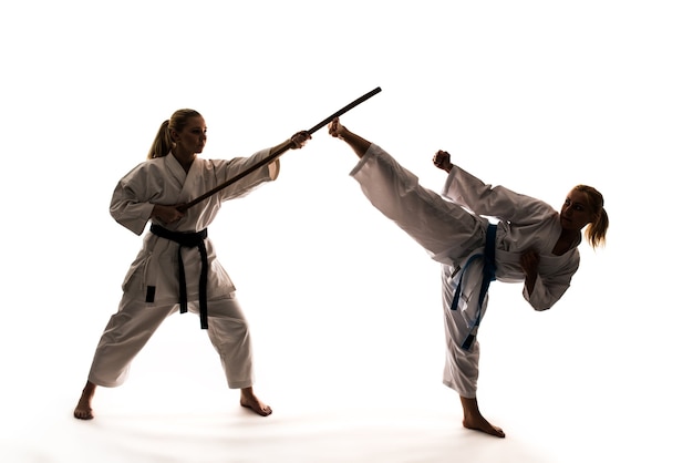 Entrenamiento de dos niñas en kimonos blancos utilizando material deportivo y soporte de karate. Aislado sobre fondo blanco