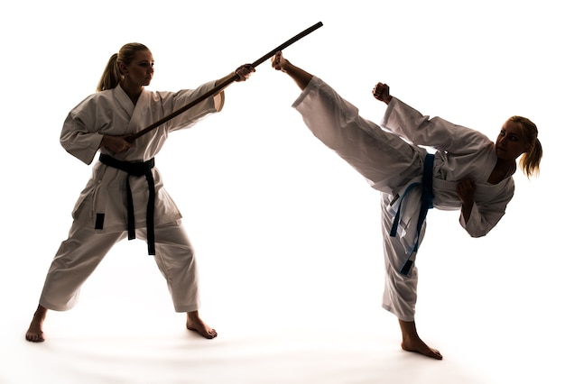 Entrenamiento de dos niñas en kimonos blancos utilizando material deportivo y soporte de karate. Aislado sobre fondo blanco