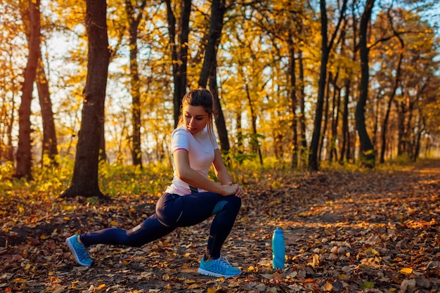 Entrenamiento y ejercicio en el parque de otoño. Joven mujer estirando las piernas al aire libre. Estilo de vida saludable y activo