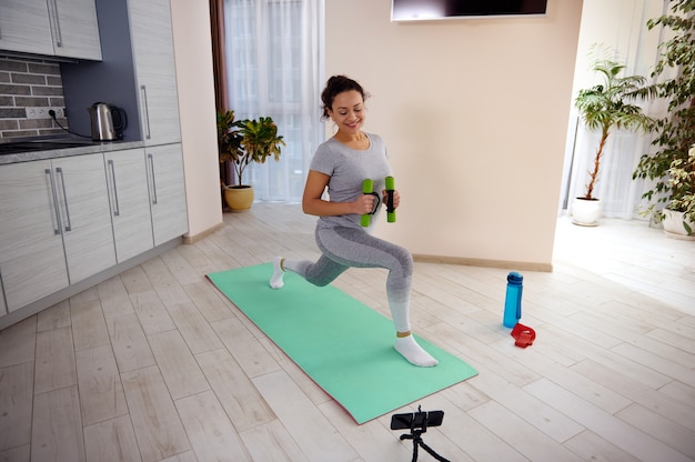 Entrenamiento de entrenamiento de una mujer fitness haciendo ejercicios de estocadas para el músculo de la pierna mientras ve tutoriales en casa