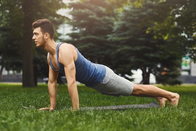 Entrenamiento del entrenamiento de la tabla del hombre de la aptitud en el parque al aire libre. Chico joven hace ejercicio. Estilo de vida saludable, concepto de gimnasia