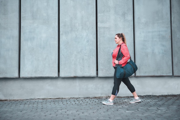 El entrenamiento es sobre la vista posterior de una mujer de talla grande en ropa deportiva que lleva su bolso