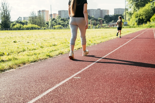 Entrenamiento en un estadio al aire libre. Mujer joven caminando sobre una cinta roja afuera, vista posterior. Estilo de vida activo, pérdida de peso.