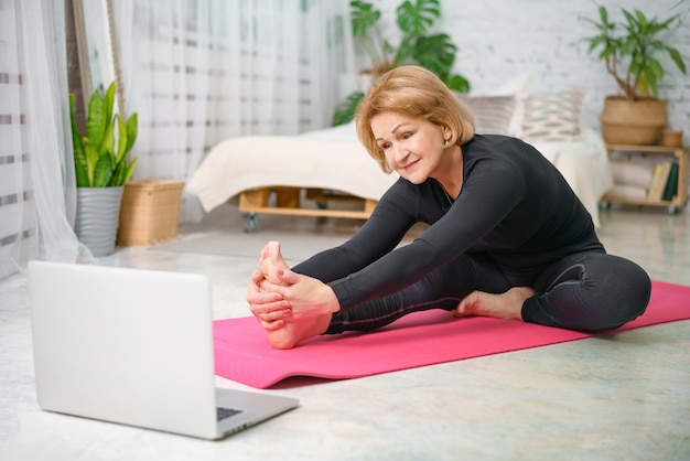 Entrenamiento físico en línea, mujer mayor en casa con la computadora portátil.