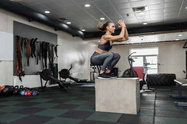 Entrenamiento funcional cruzado. Mujer en forma muscular saltando sobre una caja de madera en un gimnasio moderno