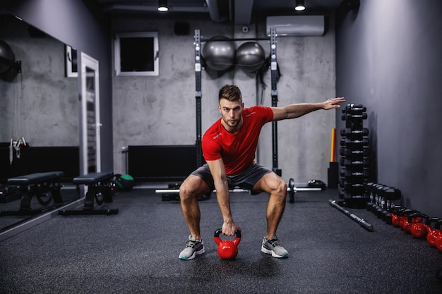 Foto entrenamiento funcional de cuerpo completo de crossfit con una campana de caldera un hombre en ropa deportiva con un rojo