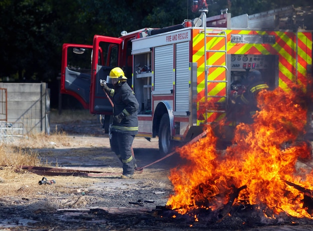 Entrenamiento de incendios y camión con bombero y emergencia en la naturaleza para la seguridad del humo y la explosión Peligro intrépido y trabajo en equipo con un grupo de hombres al aire libre para la operación y acción de rescate