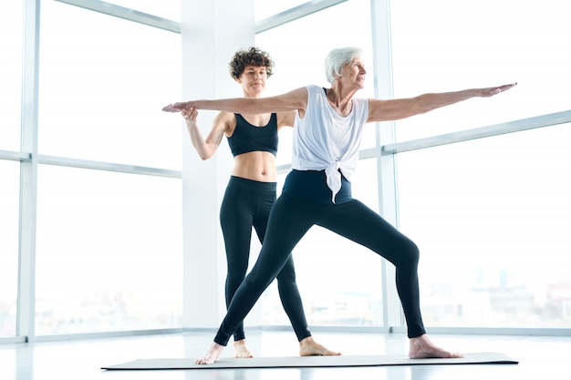 Entrenamiento con instructor. Mujeres en colchoneta haciendo yoga junto a una ventana grande