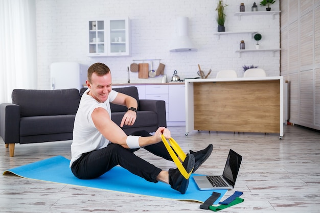 Entrenamiento en linea. Hombre haciendo ejercicio con gomas elásticas en casa, espacio libre. Hacer deporte en casa