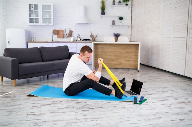 Entrenamiento en linea. Joven haciendo ejercicio con gomas de fitness con tutorial en línea en casa, espacio libre. Hacer deporte en casa