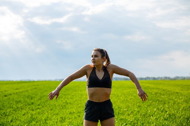 Entrenamiento de la mañana. Concepto de estilo de vida saludable. Mujer atractiva joven en ropa deportiva hace estirar la mano antes de entrenar en la naturaleza al amanecer. Calentamiento muscular