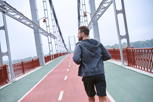 Entrenamiento matutino cerca de joven en ropa deportiva haciendo ejercicio mientras trota en el