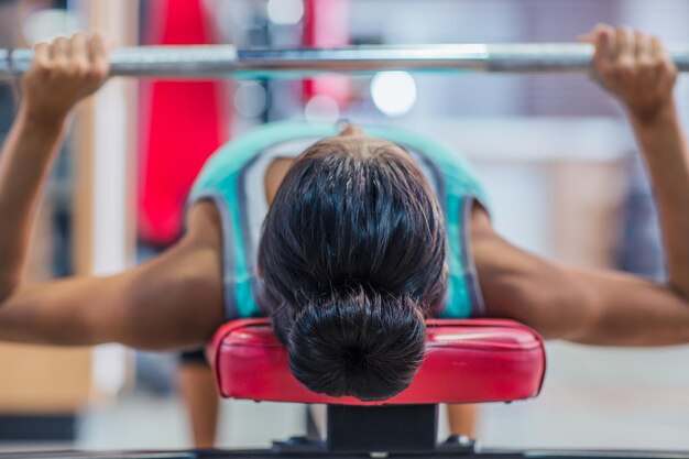 Entrenamiento de mujer joven con barra en el banco en el gimnasio