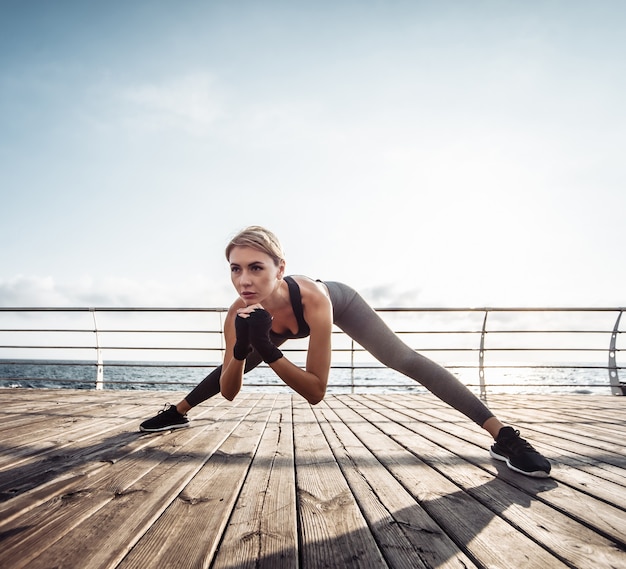 Entrenamiento de mujer sana en el paseo marítimo Joven atractiva en ropa deportiva hace estiramientos antes de hacer ejercicio en la playa al amanecer.