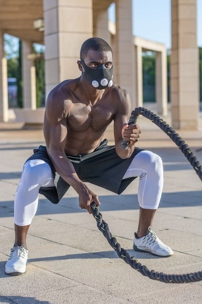 Foto entrenamiento muscular masculino con cuerdas de combate y máscara de entrenamiento.