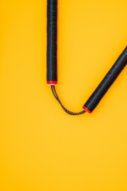 El entrenamiento de nunchaku negro está aislado en una superficie naranja