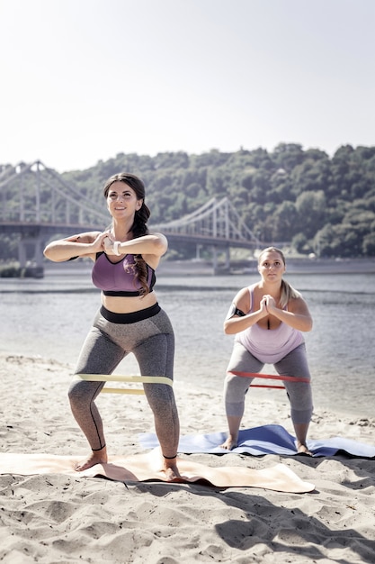 Entrenamiento productivo. mujeres positivas felices haciendo abdominales mientras usan banda elástica para entrenar