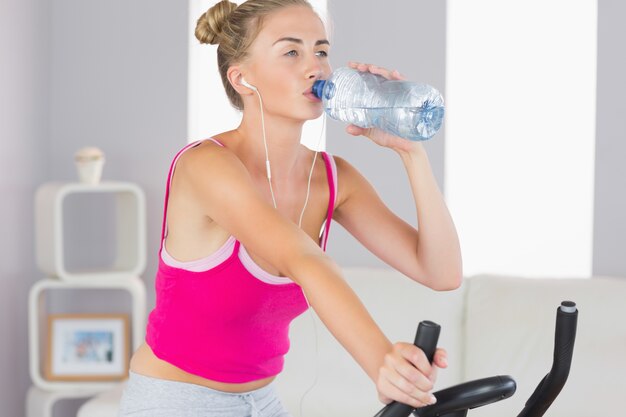 Entrenamiento rubio enfocado deportivo en agua potable de bicicleta estática