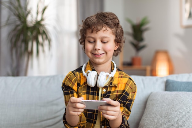 Entretenimento infantil moderno menino bonitinho jogando videogame online no smartphone em casa espaço livre