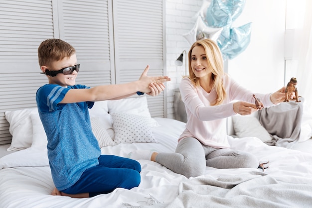 Entretenimento interessante. Jovem mãe alegre e feliz sentada na cama segurando brinquedos enquanto brincava com seu filho