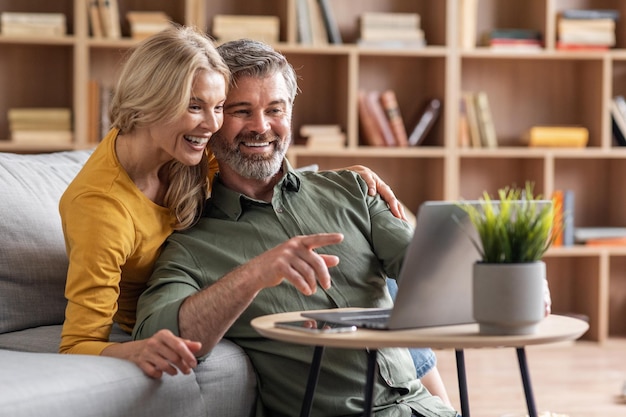 Entretenimiento digital Alegre pareja de mediana edad usando una computadora portátil en casa juntos