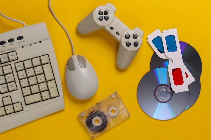 Foto entretenimiento retro. teclado antiguo, mouse de pc, discos compactos, gamepad, gafas anaglifo, casete de audio en amarillo