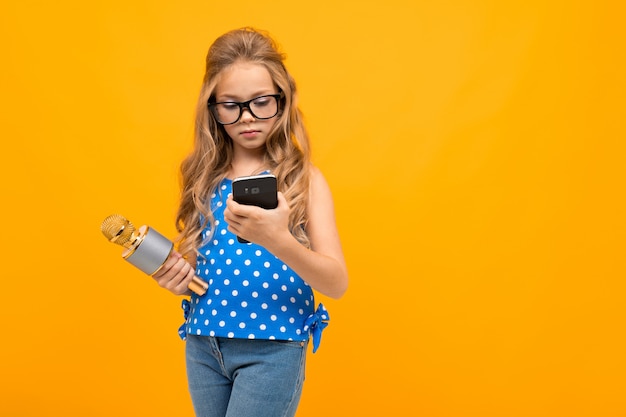 Se entrevista a una niña con gafas con un micrófono, la imagen está aislada en la pared amarilla