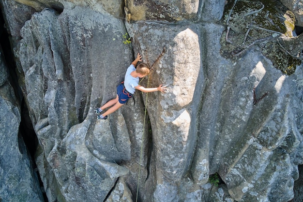 Entschlossener Junge Kletterer klettert die steile Wand des felsigen Berges hinauf. Kind überwindet schwierige Route. Engagement in Extremsportarten und Klettern Hobby-Konzept.