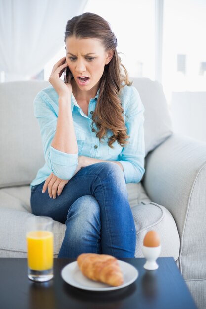 Entsetzte Frau am Telefon, das auf Sofa sitzt