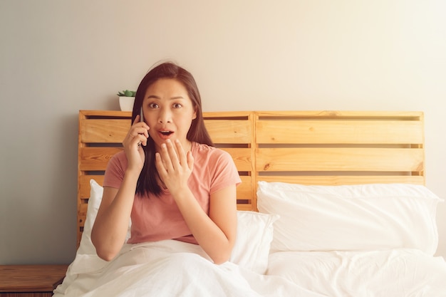 Entsetzte und überraschte Frau hat ein Telefongespräch auf ihrem Bett.