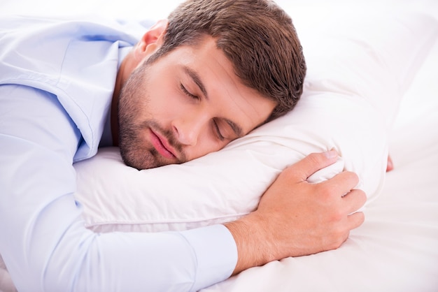 Entspannen nach einem harten Arbeitstag. Hübscher junger Mann in Hemd und Krawatte, der im Bett schläft