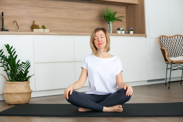 Entspannende Frau, die in einer Lotussitzposition sitzt, während sie zu Hause Yoga macht