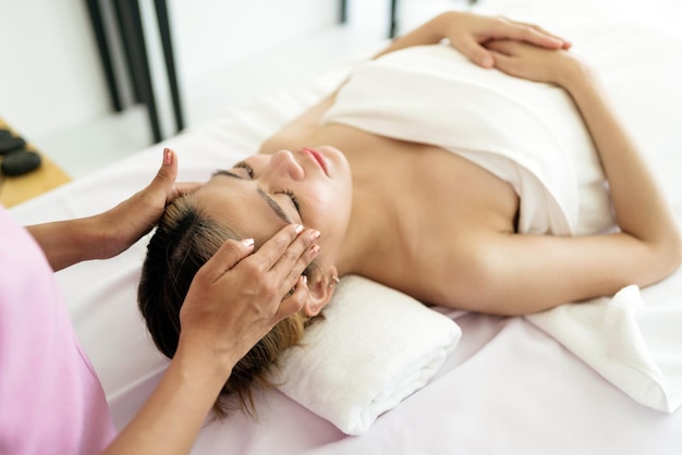 Entspannende junge asiatische Frau, die sich auf Massagebetten hinlegt und die Augen schließt, während sie eine Massage von einem Therapeuten in einem asiatischen Luxus-Spa-Salon und einem Wellness-Center erhält und auf das Spa-Salon-Konzept wartet